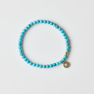 Turquoise beaded bracelet with a gold devil eye charm on a white background