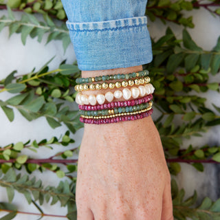 mix of red and green bracelets on wrist with greenery in background