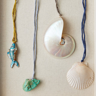 Four necklaces with shell and fish pendants on a beige fabric background