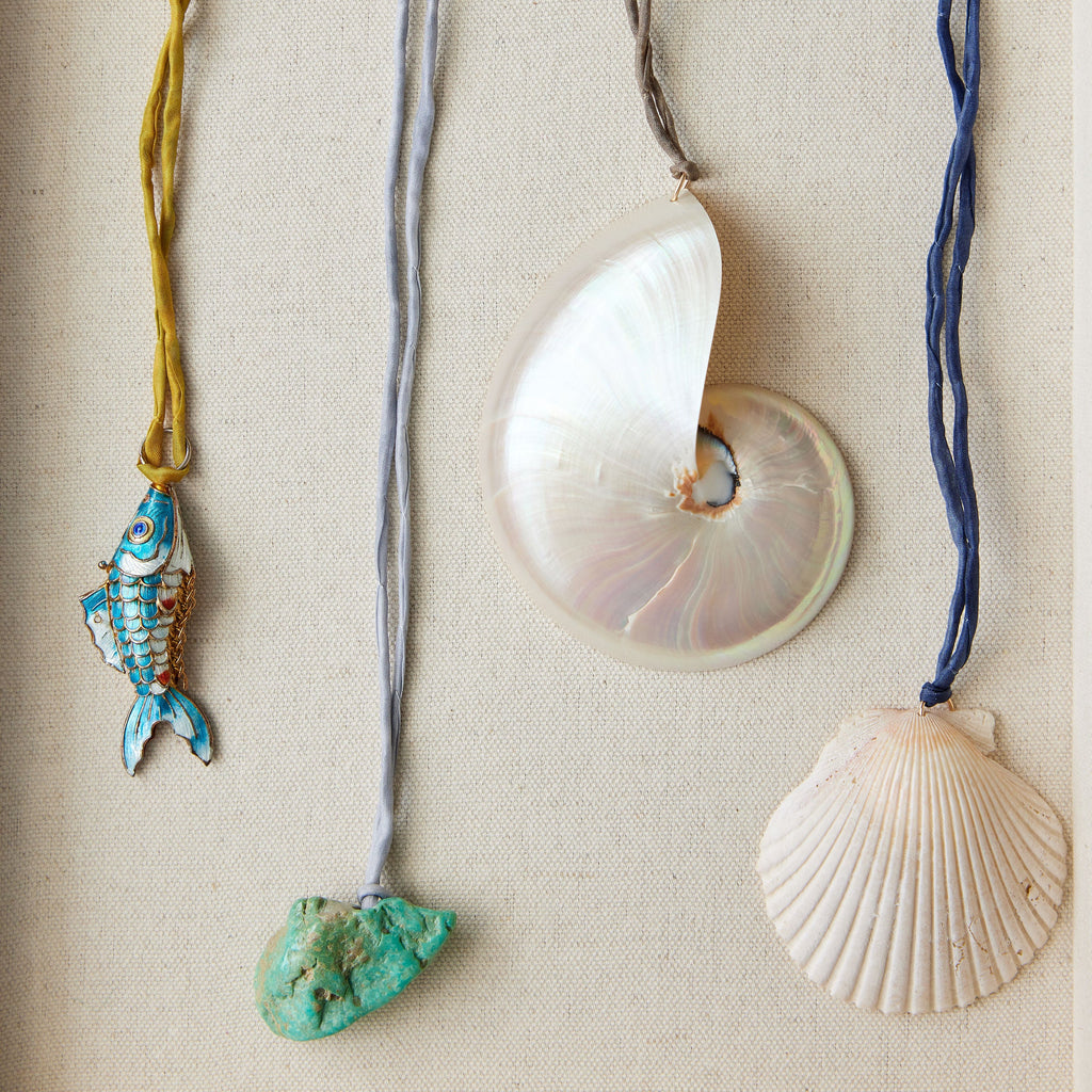 Four necklaces with shell and fish pendants on a beige fabric background