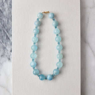 Blue beaded necklace on a white card with a marble background