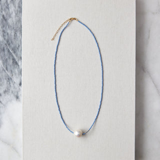 Necklace with a pearl pendant on a white card against a marble background