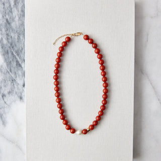 Red beaded necklace with pearl on a white card with a marble background
