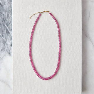 Pink beaded necklace on a white card with a marble background