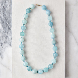 Blue beaded necklace on a white card with a marble background