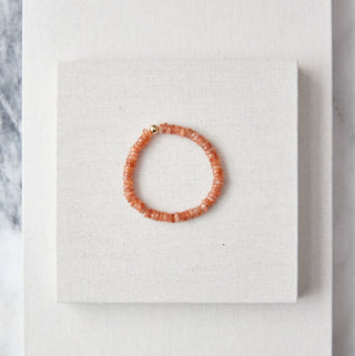 Orange beaded bracelet on a white card with a marble background