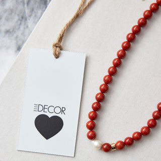 Red beaded necklace with pearl with a 'ELLE Decor' tag on a marble surface
