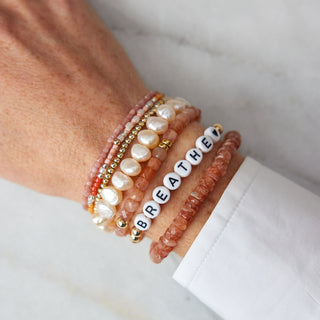 Close-up of a wrist wearing multiple bracelets with visible text on a marble surface