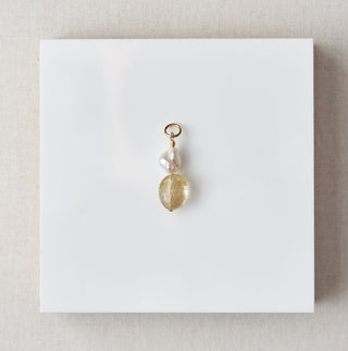 Gold pendant on a white card with beige border on a marble surface