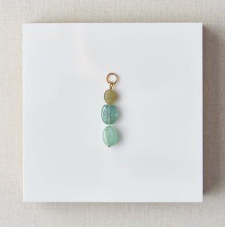 Charm with green beads on a white card against a marble background