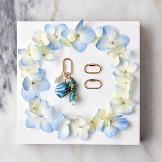 Jewelry set with charms and a carabiner on a white card with blue and white flowers, placed on a marble surface.