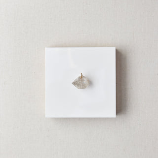 Small crystal on a white card inside a beige box on a marble surface