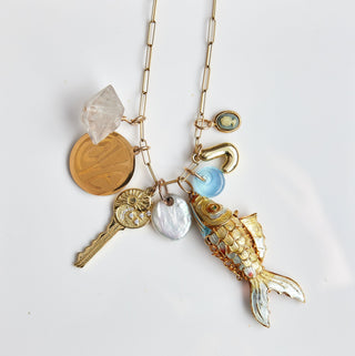 Necklace with various charms on a white card, with a jewelry dish in the foreground.