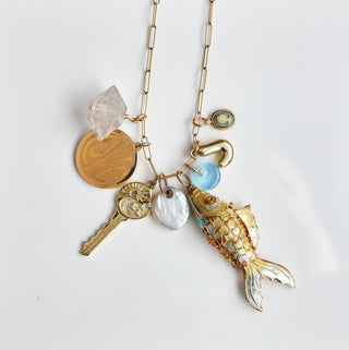 Necklace with various charms on a white card, with a jewelry dish in the foreground.