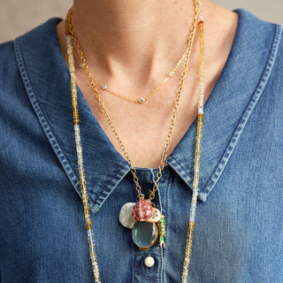 Long beaded necklace with floral charm on a blue denim shirt
