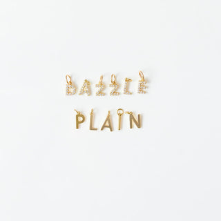 Gold charm pendants labeled 'DAZZLE' and 'PLAIN' on a white background