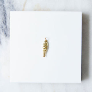 Gold fish-shaped pendant on a white card with a marble background