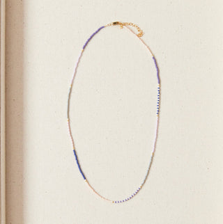 Necklace displayed in a box with decorative shells on a marble surface