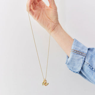 Hand holding a gold necklace with three puffy letter charms against a light gray background