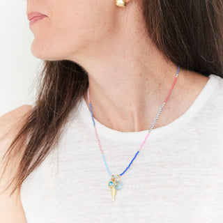 Woman wearing a necklace with colorful beads and gold earrings against a white background