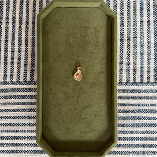 Gold oyster pendant on a green velvet display box with a striped fabric background