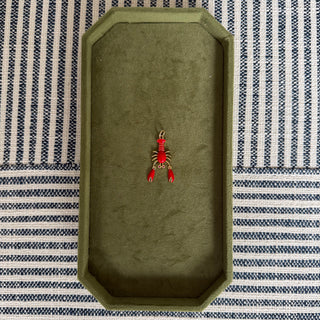 Small red lobster pendant on a green tray with a striped background