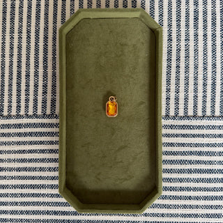 Green jewelry box with a yellow pendant on a striped fabric background