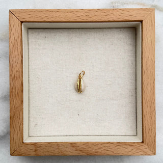 A small gold huggie hoop earring displayed inside a square light wood shadow box with a cream fabric lining, set on a white and gray marble surface.