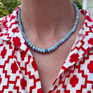A close-up of a person wearing a light blue beaded necklace with a red and white geometric patterned shirt.