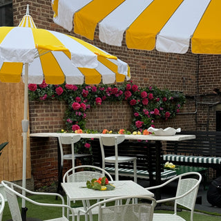 Outdoor seating area with white and yellow striped umbrellas, tables, and chairs against a brick wall.