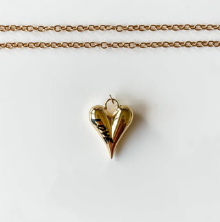 Gold heart-shaped pendant necklace on a white card with a marble background