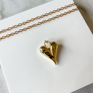 Gold heart-shaped pendant necklace on a white card with marble background