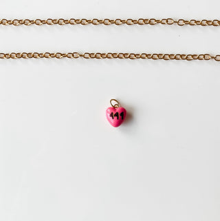 Gold chain bracelet with a pink heart charm on a white card against a marble background