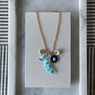 Necklace with a blue eye charm on a gray card, framed by a striped fabric border.
