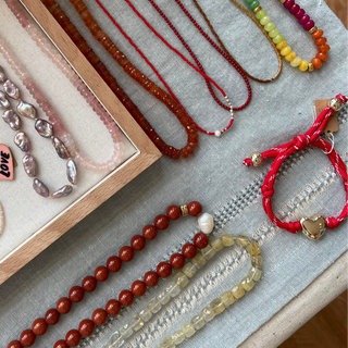 Collection of beaded necklaces and bracelets on a textured surface with a box.