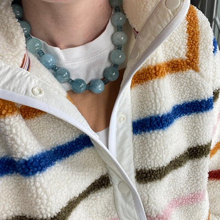 Close-up of a person wearing a colorful striped sweater and a blue beaded necklace.