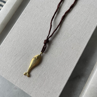 Brass fish pendant on a brown cord against a light gray background