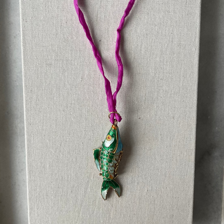 Green pendant on a purple cord displayed on a white card with a gray background