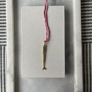 Small gold fish pendant on a pink thread against a gray background