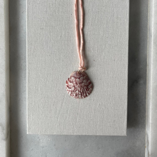 Necklace with a shell pendant on a gray card inside a gray frame.