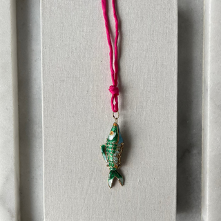 Green fish-shaped pendant on a pink cord against a gray background