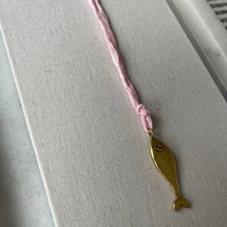 Gold fish-shaped pendant on a pink string against a white background