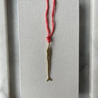 Brass fish-shaped pendant on a coral string against a gray background