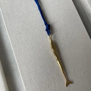 Gold fish-shaped pendant on a blue cord against a gray background
