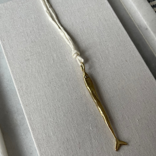 Gold fish-shaped pendant on a white cord against a gray background