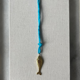 Brass fish charm on a blue string against a textured gray background
