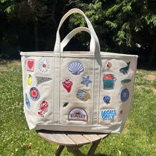 Beige tote bag with various patches on a wooden stool outdoors.