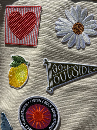 Collection of embroidered patches on a fabric background, including a heart, daisy, lemon, and 'Go Outside' design.