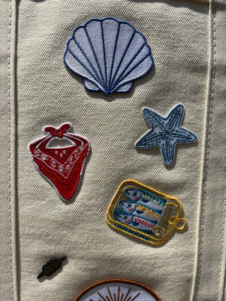 Set of embroidered patches including a shell, bandana, starfish, and can on a fabric background.