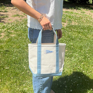 Person holding a white tote bag with blue straps outdoors on grass